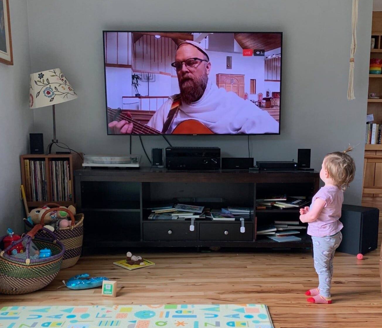 Toddler watching Rabbi Eli's service on big screen on Zoom